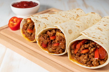 Tasty homemade burrito with vegetables and beef on wooden background.