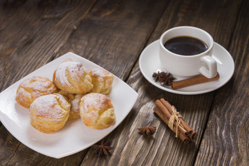 Delicious eclairs sprinkled with icing sugar, stand on a wooden table. Copy spase.