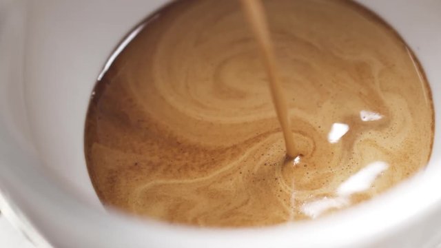 Slow motion handheld shot of coffee brew in cappuccino cup from above