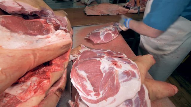 A male butcher is cutting skin and some pieces off the slab of meat