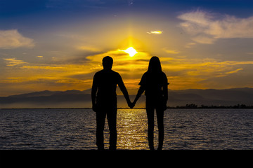 Silhouette of men and women who hold hands, on the seaside at sunset