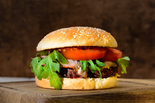 Delicious tasty burger with beef, tomatoes, salad and sauce on board on wooden  background, close-up