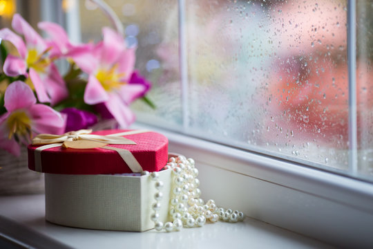 Open gift box with white pearl necklace near near window with raindrops in the daylight