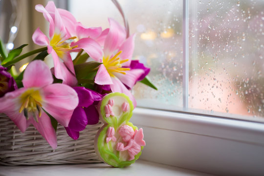 Decorative figure eight and tender bouquet of beautiful pink tulips in white basket near window with raindrops in the daylight