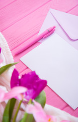 Clear sheet of white paper with pen and envelope and tender bouquet of beautiful tulips on pink wooden background