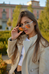 Mujer vestida a la moda con gafas de sol posando delante de un palacete en la ciudad