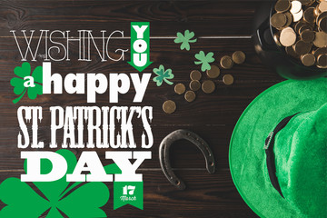 flat lay with horseshoe, hat and pot of gold on wooden tabletop with wishing you a happy st patricks day lettering