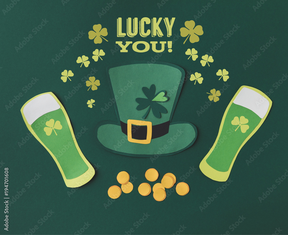 Wall mural flat lay with glasses of beer, coins, green hat, shamrocks and lucky you lettering on green background