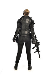 full length portrait of female  soldier wearing black  tactical armour, standing  with back to the camera holding a gun, isolated on white studio background.