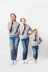 Fototapeta premium mother and daughters in similar clothing talking on smartphones isolated on grey