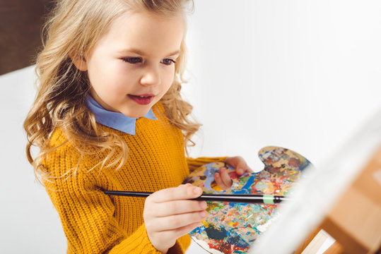close-up shot of little child painting on canvas with oil paint on white