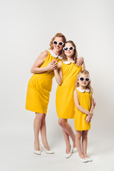 mother and daughters in similar retro style yellow dresses and sunglasses on white