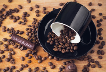 coffee beans in a mug next to a chocolate candy on a wooden surface