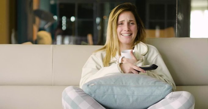 A woman relaxes on the sofa at home, hugging a pillow and watching a movie in canvas and smile. Concept of: leisure, relax, tv.