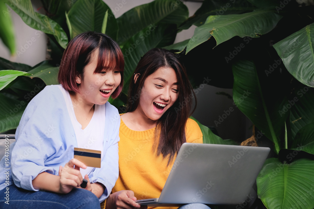 Wall mural two asia woman excited with sale promotion on website shop on laptop sitting on chair in garden at h