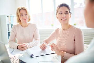 Two businesswomen listening to their associate during discussion of financial information