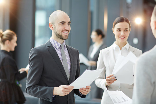 Happy Young Traders With Business Documents Consulting One Of Clients At Meeting