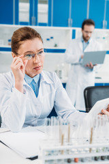 selective focus of female scientist using tablet at workplace with colleague behind in lab