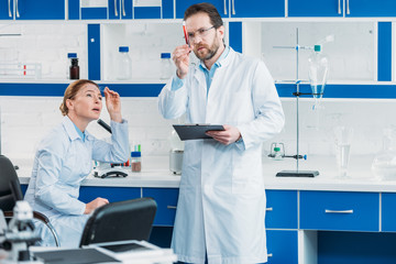 scientific researcher looking at flask with reagent in hand with colleague near by in laboratory