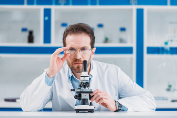 portrait of scientist in white coat and eyeglasses with microscope in laboratory