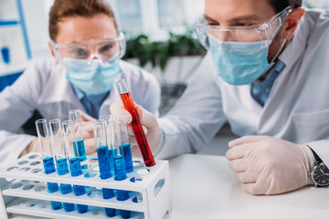 selective focus of scientific researchers in goggles and medical masks looking at reagents in tubes in lab