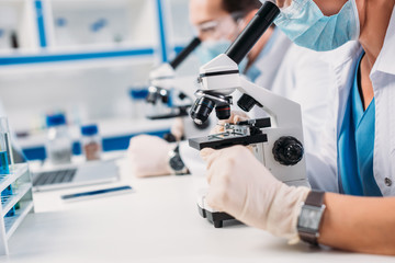 selective focus of scientists in medical masks and goggles looking through microscopes on regents in lab