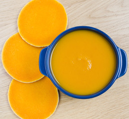 Pumpkin soup in a blue bowl and round pieces of pumpkin on wooden background