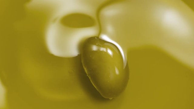 Slow motion closeup olive falls in extra virgin olive oil