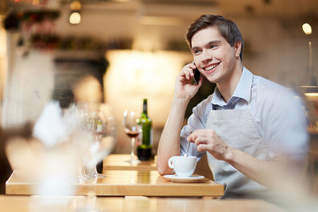 Young waiter talking on the phone during his coffee break at work