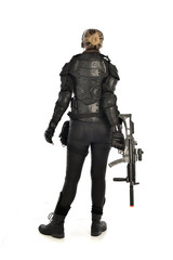 full length portrait of female  soldier wearing black  tactical armour, standing  with back to the camera holding a gun, isolated on white studio background.