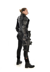 Fototapeta premium full length portrait of female soldier wearing black tactical armour, standing with back to the camera holding a gun, isolated on white studio background.