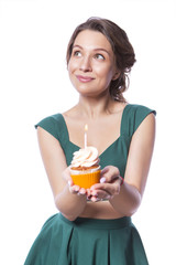 Brunette pretty beautiful caucasian woman in green festive dress blowing candle on a birthday party cupcake. Isolated white background