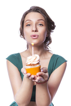 Brunette pretty beautiful caucasian woman in green festive dress blowing candle on a birthday party cupcake. Isolated white background