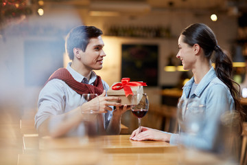 Young happy couple celebrating their anniversary. Man giving a present to the girl