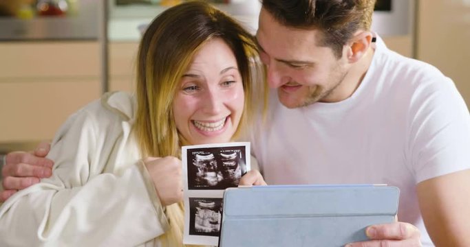 A married couple in love videocall their parents using a tablet, to announce the birth of their son showing the ultrasound. Concept of: family, birth, life, love