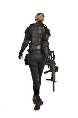 full length portrait of female  soldier wearing black  tactical armour, standing  with back to the camera holding a gun, isolated on white studio background.