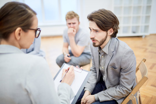 Troubled young businessman explaining his problem to counselor during group session