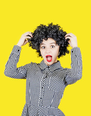 Happy girl with big black hair with an expression of surprise from the news, isolated on a yellow background