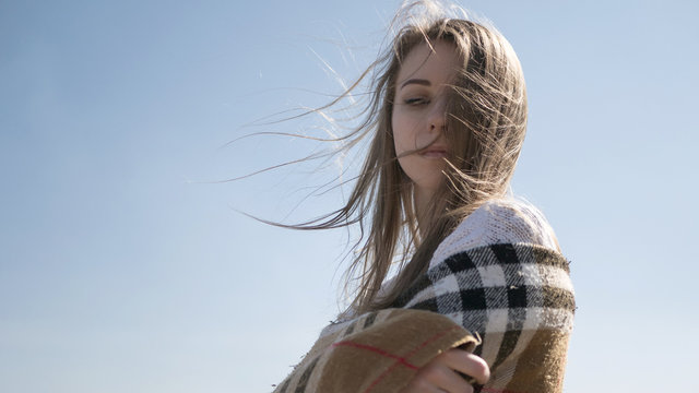 Beautiful young teenage caucasian woman in a plaid walking thinking a bit sad in a park near river (lake) in spring (autumn) cold windy weather. lifestyle portrait in nature. Copy space