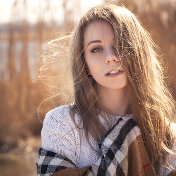 Beautiful young teenage caucasian woman in a plaid walking thinking a bit sad in a park near river (lake) in spring (autumn) cold windy weather. lifestyle portrait in nature. Copy space