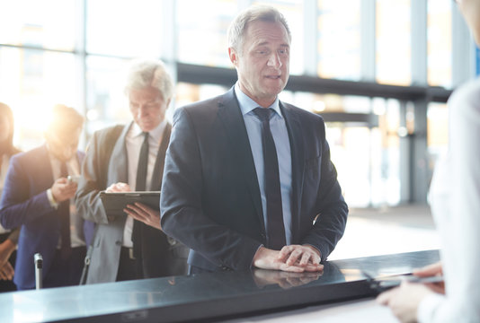 Mature traveler standing by check-in counter and answering questions of administrator