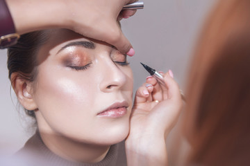 Professional make up artist apply mascara to a young caucasian woman on her date and wedding photosession. Indoors, studio. Casual outfit. Backstage of a process