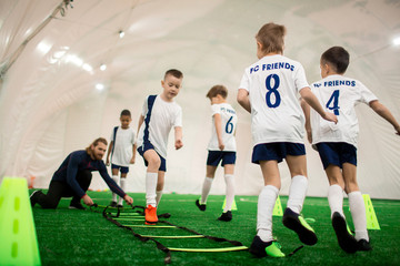 Fototapeta premium Football team of adorable boys exercising on green pitch on special facilities