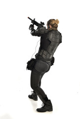 full length portrait of female  soldier wearing black  tactical armour, standing  with back to the camera holding a gun, isolated on white studio background.