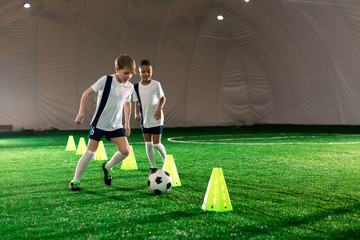 Fototapeta premium Two little football players running after ball while exercising on pitch with cones
