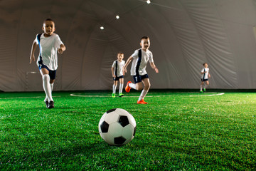Several little football players running sfter soccer ball down green field