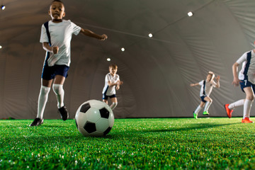 Soccer ball on green pitch and little players running towards it during game