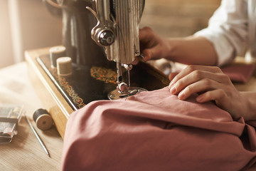 Sewing keeps my mind relaxed. Cropped shot of female tailor working on new project, making clothes with sewing machine in workshop, being busy. Young designer making her ideas come true - obrazy, fototapety, plakaty