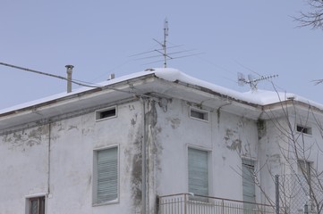Ruined old house with blue window and snowy roof (Pesaro, Italy)