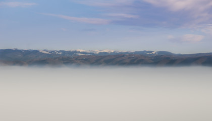 Gentile, eroded, snow covered mountain peaks with blue sky above them and a sea of fog in the valley below